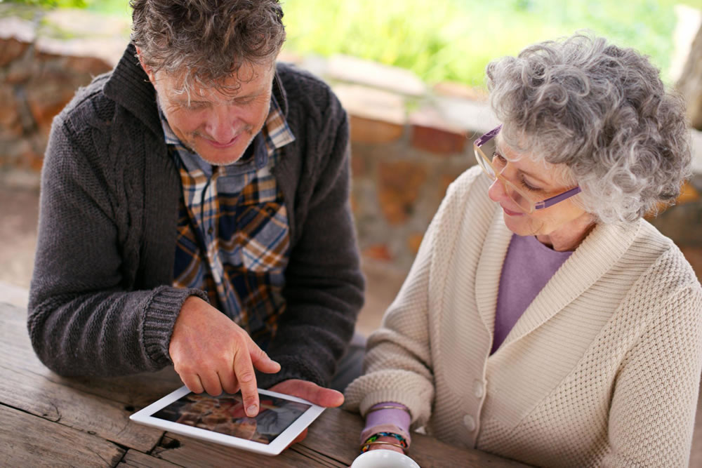 Dos personas mayores compartiendo contenido en una tablet sobre una mesa de madera en un espacio exterior
