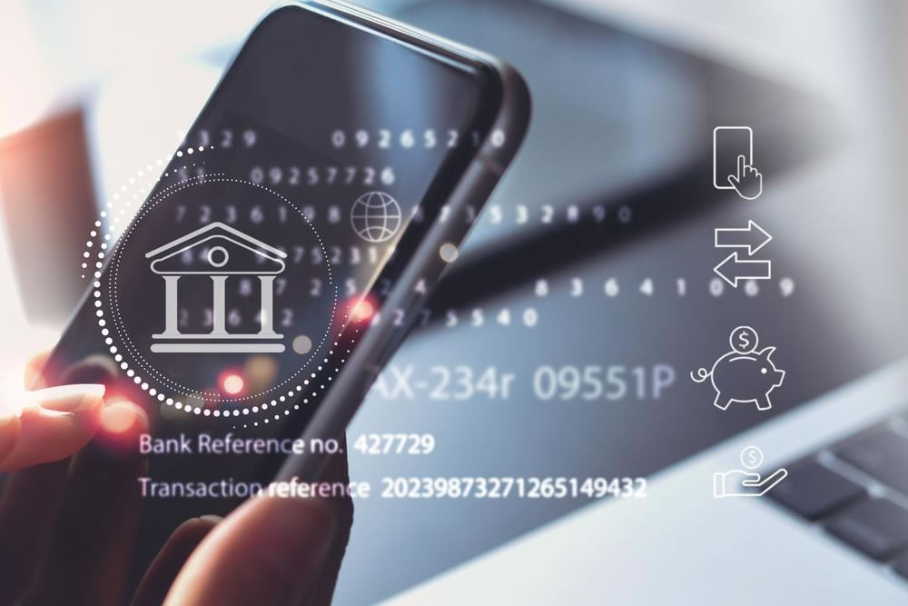 Manos usando un smartphone con iconos holográficos de banca digital, transferencias y ahorro sobre un portátil