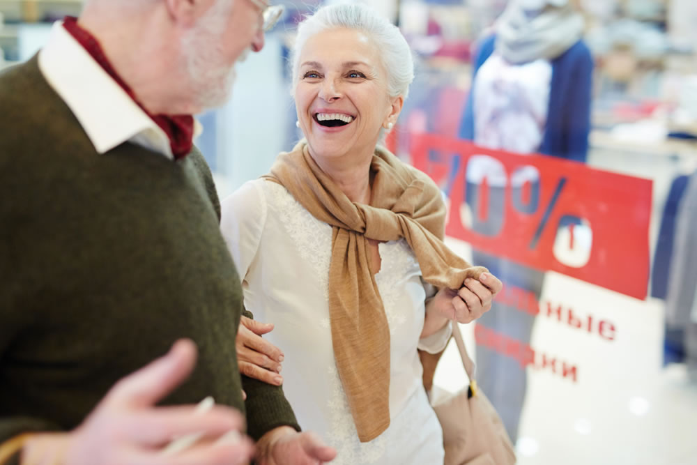 Mujer mayor sonriendo junto a un hombre en una tienda de ropa con carteles de descuento al fondo