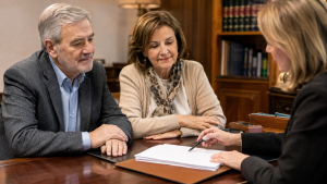 Matrimonio mayor escucha a la notaria mientras firma su testamento